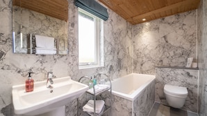 Un baño con pared de mármol, un lavabo, una bañera y un inodoro.