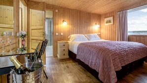 Un dormitorio de cabaña de madera con cama, lámparas de noche, mesita de noche, cómoda y ventana con cortinas.