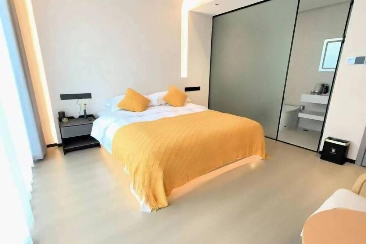 Moderni hotellihuone, jossa on sänky, yöpöytä ja suuri peili.