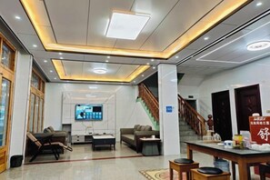 A hotel lobby with a reception desk, seating area, television, and a staircase. - Shuxiang Farmhouse (Yushan)