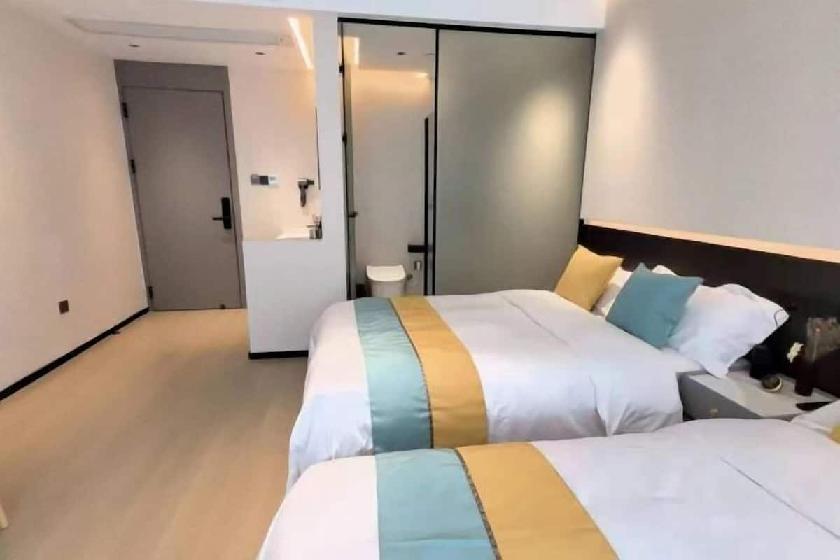Hotellihuone, jossa on kaksi sänkyä, vaatekaappi, yöpöytä ja pieni kylpyhuone.