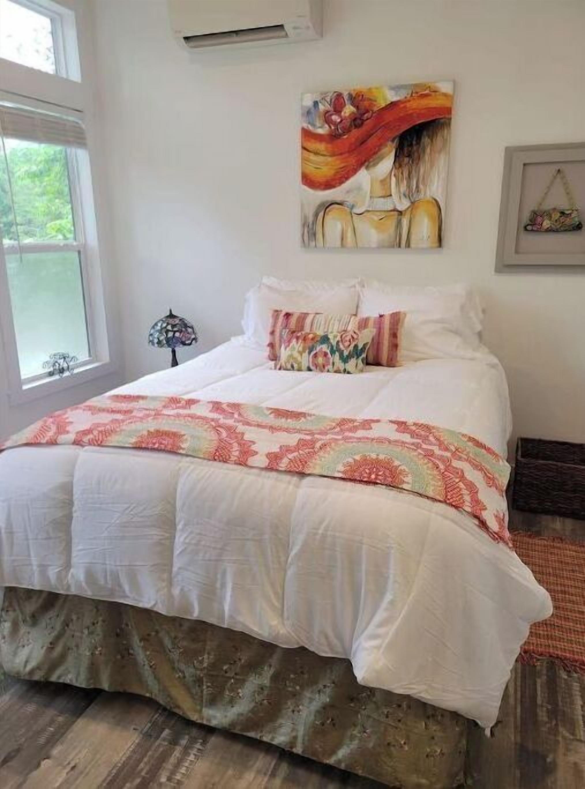 Une chambre avec un grand lit, une fenêtre et un tableau accroché au mur.