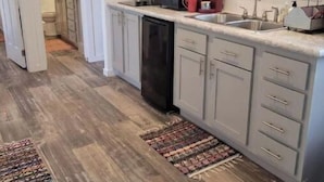 A kitchen with grey cabinets, a black dishwasher, and a window with a view of trees.