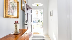 A hallway with a wooden dresser, framed artwork, and a door leading outside. - 'Morning Star Villa Spacious 4 bed with Salt Water Pool & Games Room! (Clermont)