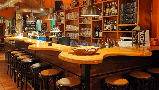 Una zona de bar con taburetes, barra, estanterías con botellas y sistema de ventilación.
