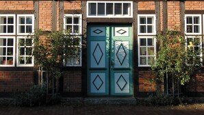 Un edificio tradicional de entramado de madera con techo de tejas, múltiples ventanas y una puerta verde con diseños de diamantes.