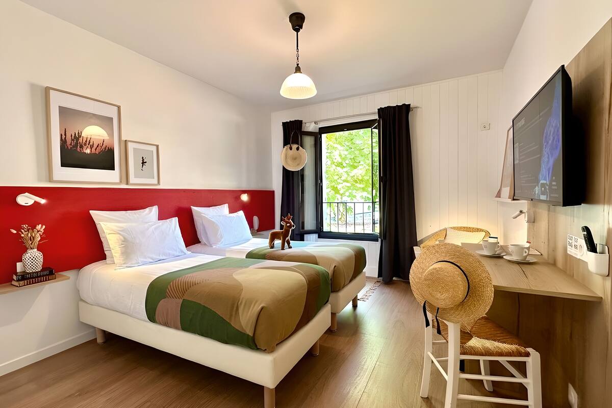 A hotel room with two beds, a desk with a chair, a television, and a window with curtains.