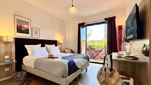 A hotel room with a bed, bedside table, lamp, and a view of the outdoors. - Hotel Le Provence - Restaurant Le Styx (La Palud-sur-Verdon)