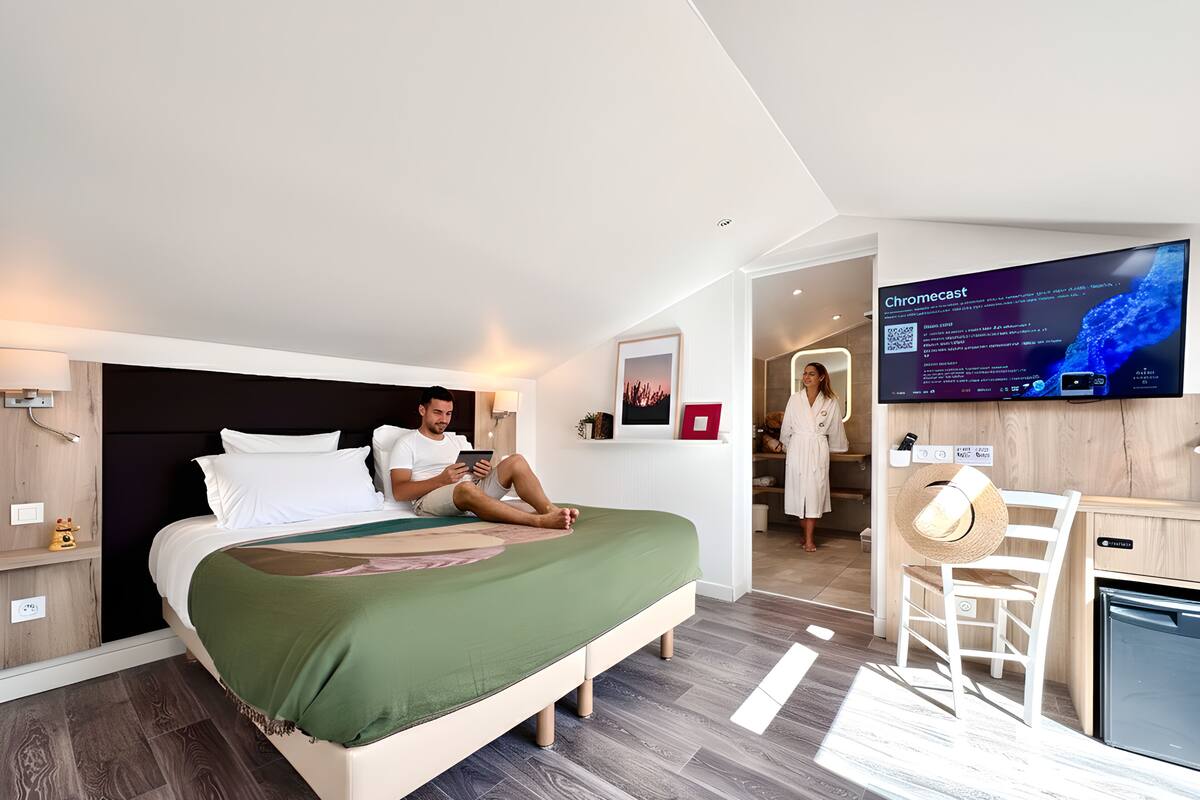 A modern hotel room with a bed, a television, a desk, and a bathroom.