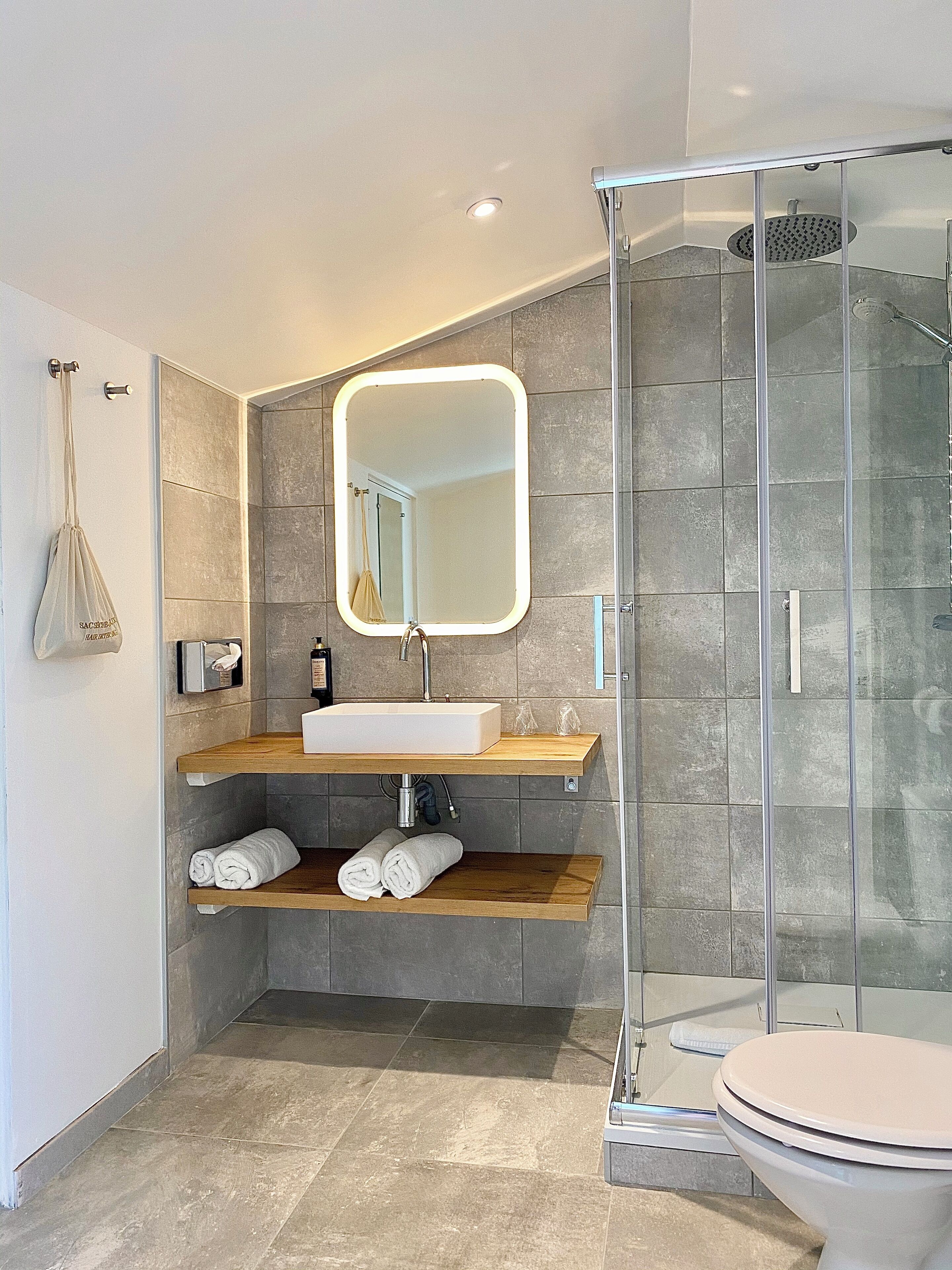 Une salle de bain moderne avec une douche à parois de verre, un lavabo blanc doté d’un plan de toilette en bois et un grand miroir.