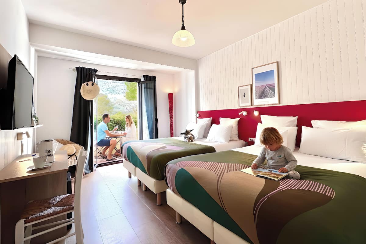 A hotel room with two beds, a desk with a chair, a TV, and a window with curtains.