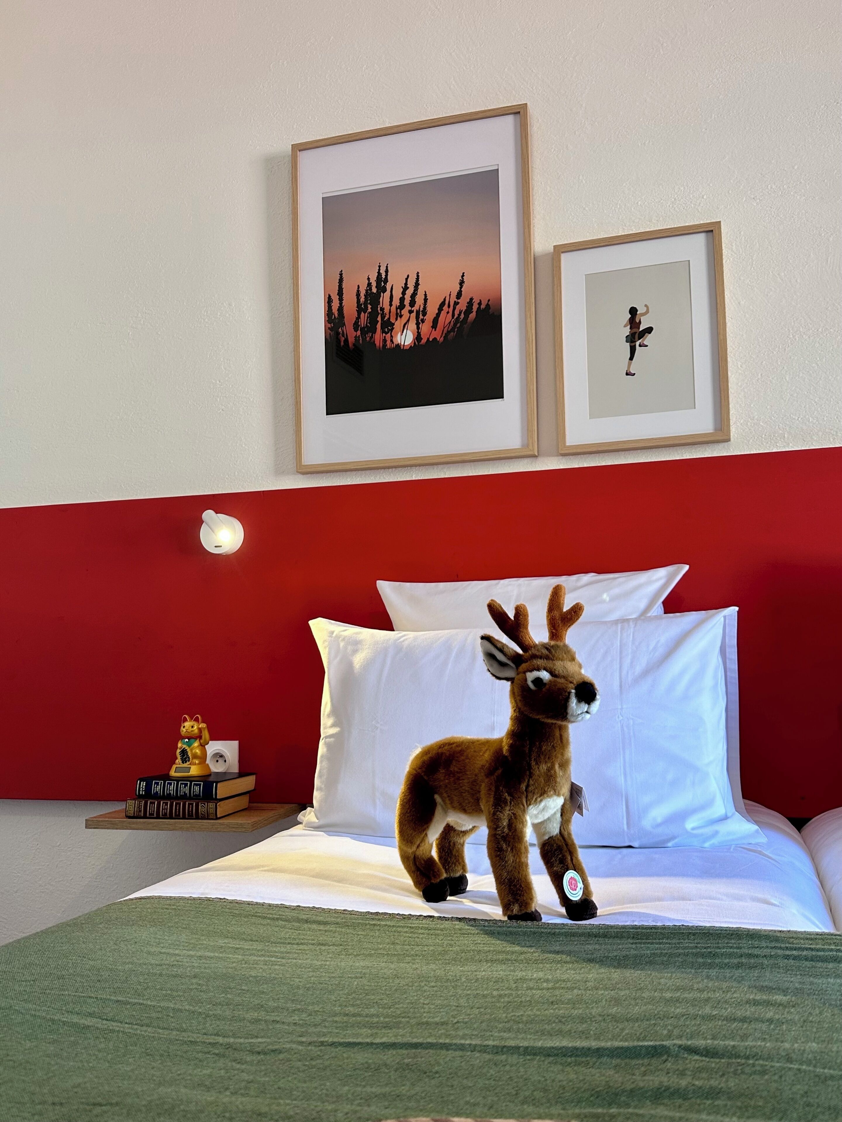 Un lit avec une literie blanche, un ours en peluche, des photos encadrées accrochées au mur et une petite table avec des livres et un objet décoratif.
