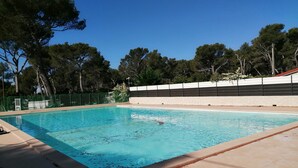A rectangular swimming pool with clear blue water, surrounded by a tiled deck and a low fence. - 2-BEDROOM CHALET IN SUNNY PROVENCE (LE CASTELLET)