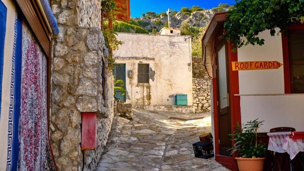 A narrow stone-paved alley with a building labeled "ROOF GARDEN" on the right.