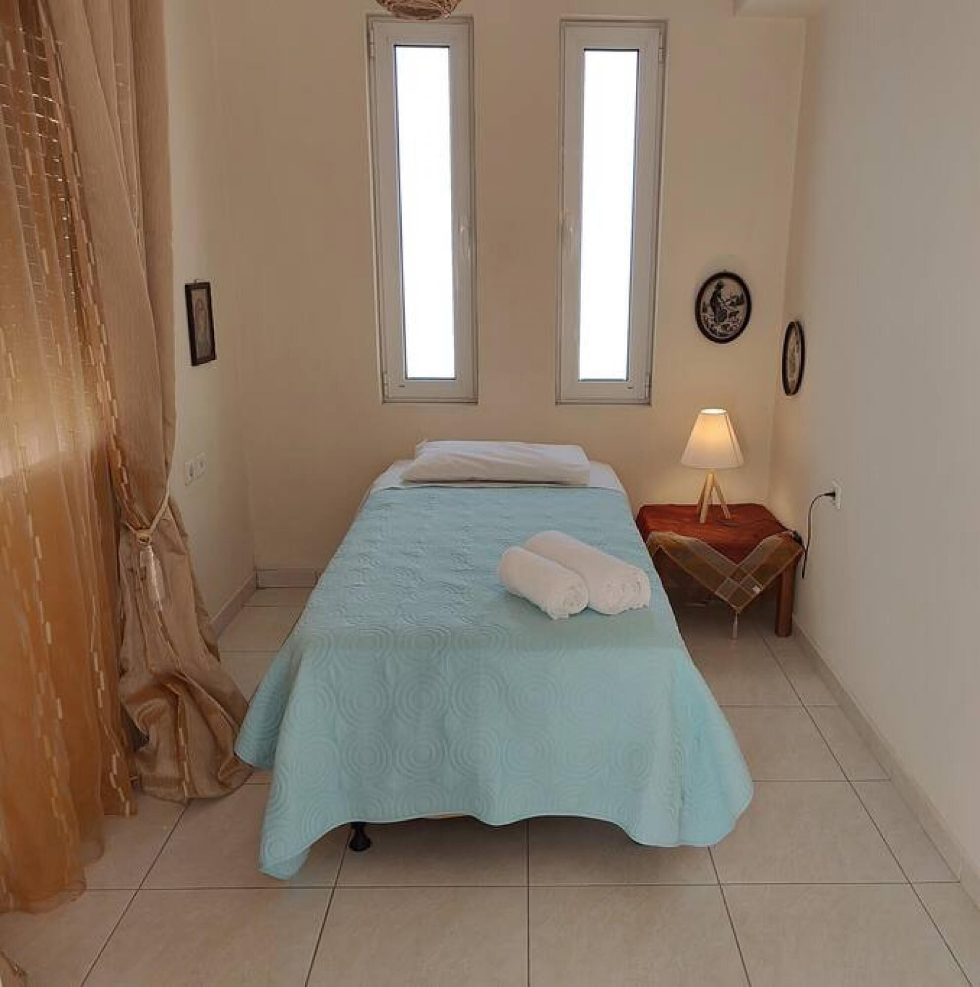 Una camera da letto con un letto, due finestre, un comodino, una lampada e una tenda.