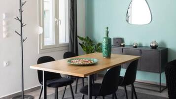A dining area with a wooden table, black chairs, a grey patterned rug, a tall floor lamp, a green vase, and a grey cabinet with decorative items.