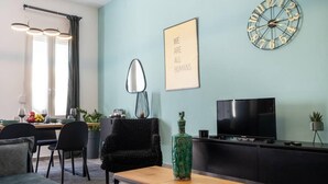 Un salon moderne avec un canapé, une table basse, un téléviseur, une horloge et une citation encadrée accrochée au mur.
