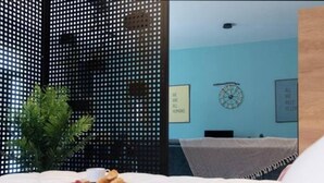 Une chambre à coucher avec un lit, une petite table sur laquelle se trouve un plateau de nourriture, une plante en pot et une horloge murale.