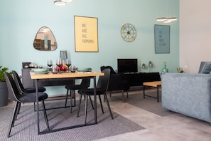 A modern living room with a dining area, featuring a sofa, a TV, and a dining table with chairs. - Casa d oro 56 Living in Paradisi Rhodes (Rhodes)