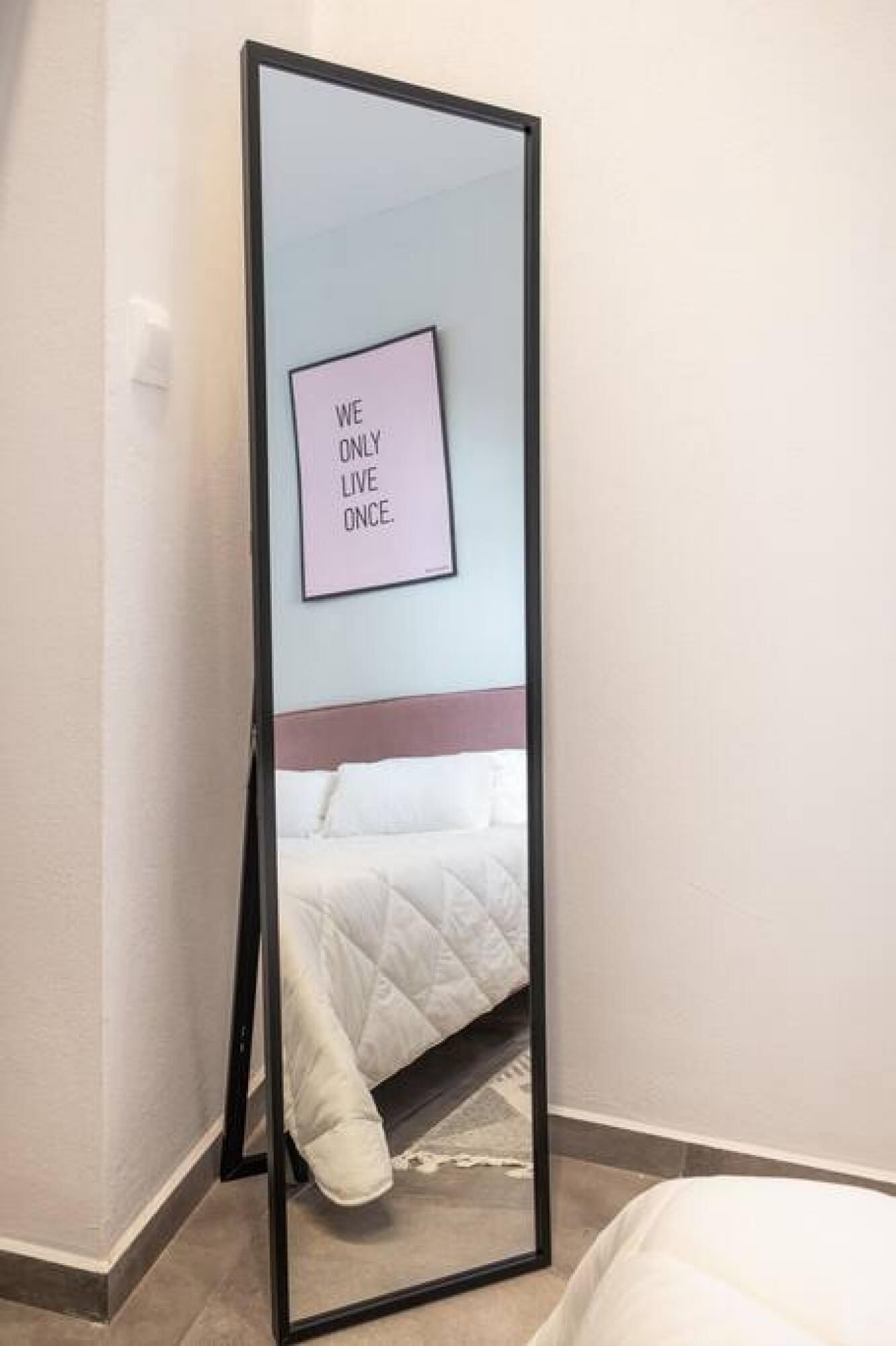 Una stanza con un letto, uno specchio grande e una citazione motivazionale sulla parete.
