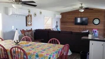 A compact living space with a dining area, a sofa, a TV mounted on the wall, and a clock.