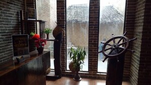 Habitación con mostrador de recepción de madera, planta en maceta, timón de barco y vista a través de un ventanal grande.