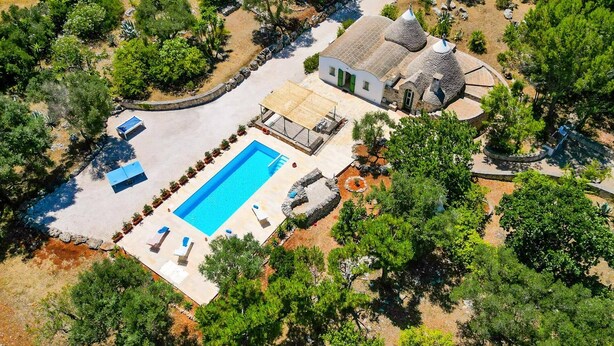 Ein Luftbild eines Anwesens mit Swimmingpool, überdachter Terrasse und einem Haus mit Steinbauweise und Kegeldach.
