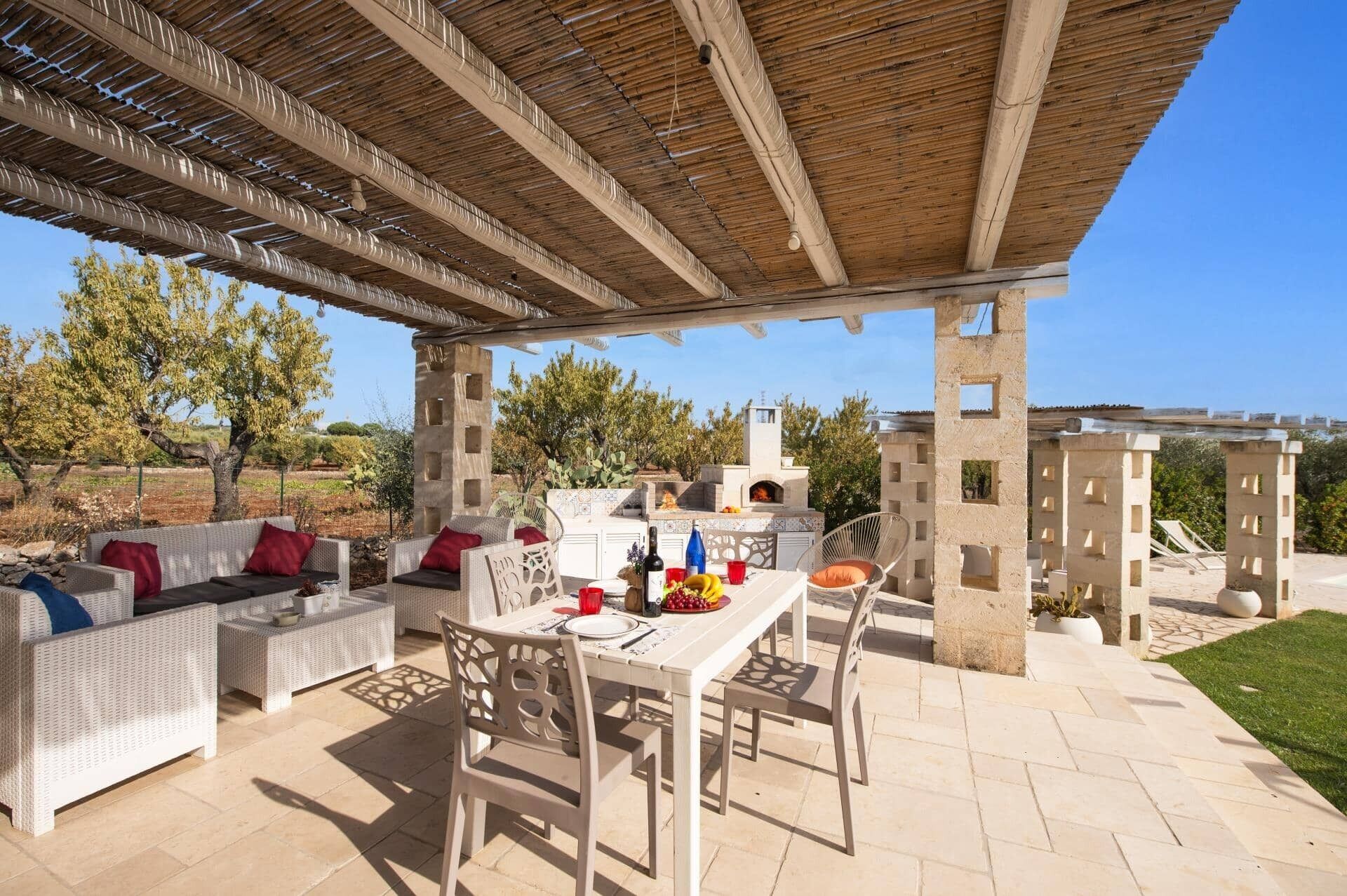 An outdoor patio with a table and chairs, a built-in grill, and a seating area with cushions.