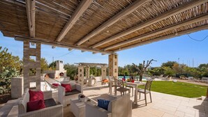 An outdoor patio with wicker furniture, a pergola, and a view of a pool and garden.