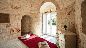 A room with stone walls, a bed with a red blanket, a dresser, and a door leading outside.