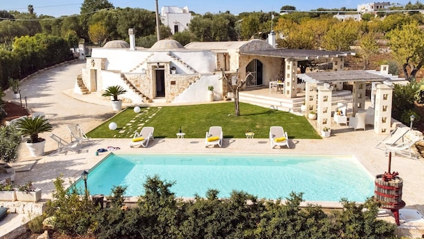 A villa with a swimming pool, outdoor seating, and a stone staircase leading to the entrance.