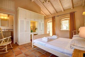 Cozy retreat with a large bed, wardrobe, and bedside table, plus a comfortable rocking chair and a window with curtains.