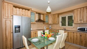 Eine Küche mit Holzschränken, einem Edelstahlkühlschrank, einem Glastisch mit Stühlen und einer Pendelleuchte.
