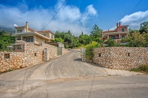 Un camino rural que conduce a una propiedad con muros de piedra, con una casa a la izquierda y un edificio a la derecha.