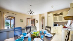 Een eethoek met een tafel voor vier personen, een bank en een keuken op de achtergrond.