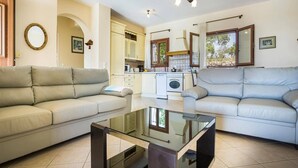 Una sala de estar con dos sofás, una mesa de centro de vidrio, una zona de cocina con lavadora y una zona de comedor con mesa y sillas.