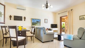 Una sala de estar con sofá, sillones, televisor y comedor con mesa y sillas.