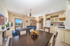 A modern living room with a dining table, blue sofa, and a fruit bowl.