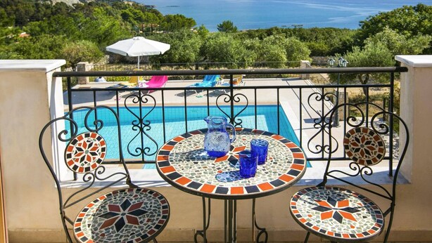 Zona junto a la piscina con vista al mar, una mesa con sillas de cerámica y una valla decorativa.