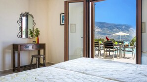 Un dormitorio con cama, escritorio, silla, espejo y vistas a un espacio exterior con mesas y sillas.