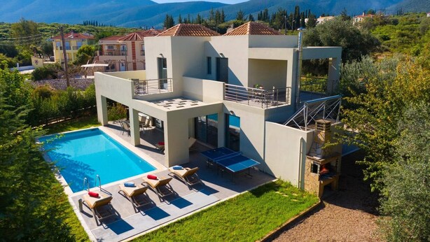 Une villa moderne à deux étages, dotée d’une piscine, d’un espace salon extérieur et offrant une vue sur les collines environnantes.