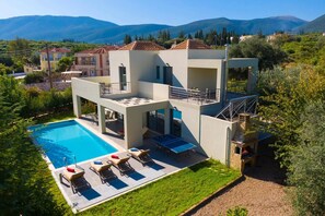 A modern two-story villa with a swimming pool, outdoor seating, and a view of the surrounding hills. - Villa Roses by Villa Plus (Karavomylos)