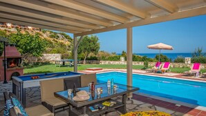 A poolside area with a covered seating area, a pool, and a view of the ocean.