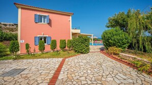 A pink building with blue shutters, a stone-paved pathway, and a pool area.