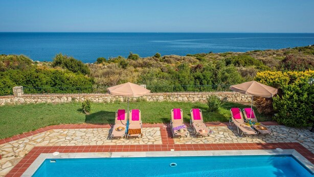 A poolside area with lounge chairs and umbrellas, overlooking a clear blue sea.