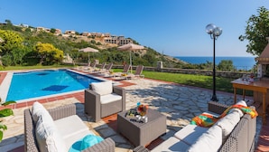 A poolside area with lounge chairs, a stone patio, and a view of the sea. - Villa Skala Ionian by Villa Plus (Ionian Islands)