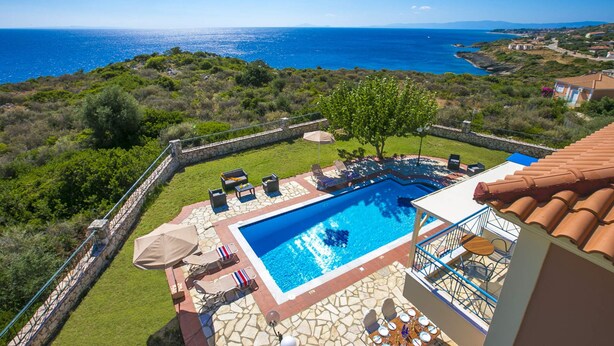 Piscina com vista para o mar, rodeada por um deck de pedra e espreguiçadeiras.