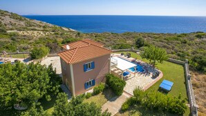 Uma casa de dois andares com telhado de cerâmica, piscina e vista para o mar.