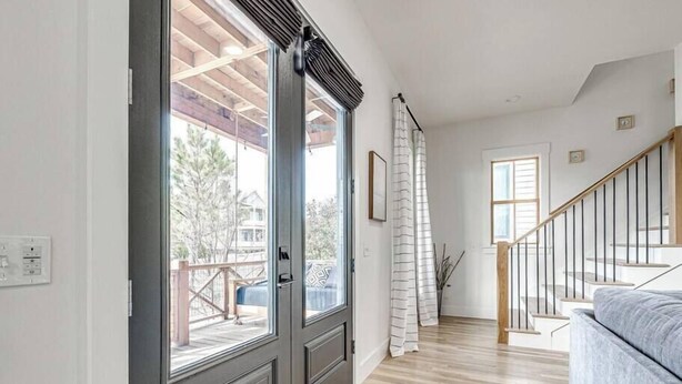 A hallway with a wooden floor, a gray couch, a staircase, and a door leading to an outdoor area.