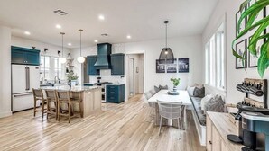 A modern kitchen with a central island, dining area with a table and chairs, and a seating area with a sofa.